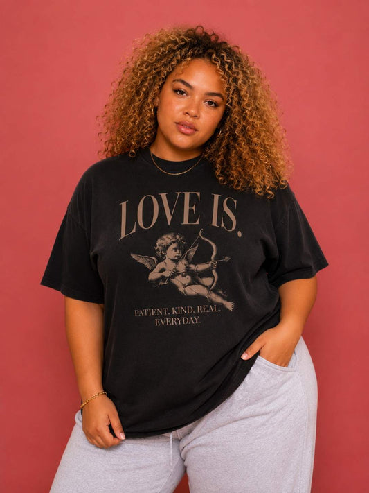 Female model wearing a vintage oversized Cupid graphic tee featuring the "Patient. Kind. Real. Everyday." love is. design